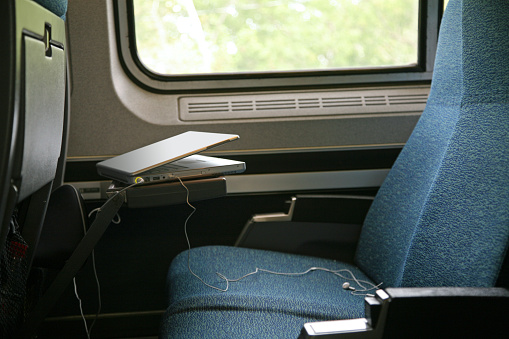 Laptop and stereo plugs on empty train seat.