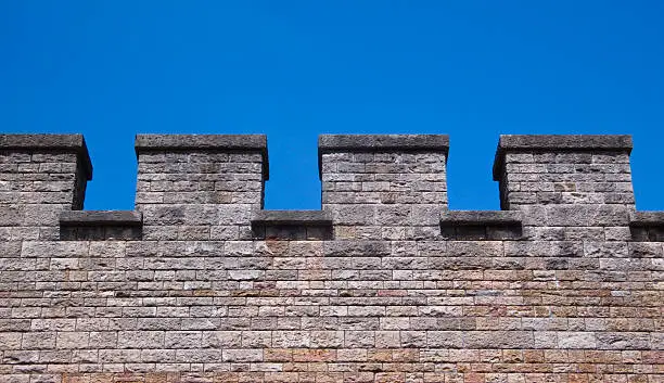 Detail of the battlements at the top of castle walls at Cardiff Castle, against a blue sky background