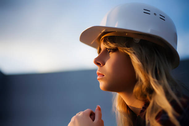 beautiful caucasian blond girl in white safety building helmet looking at sunset
