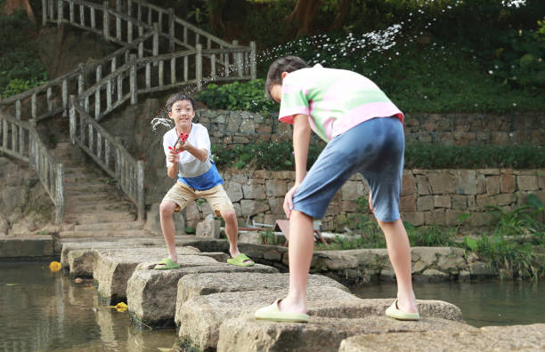 A joyful scene of a young woman and a boy splashing water at a park fountain surrounded by greenery and sunlight. The image captures happiness, playfulness, and a connection with nature.