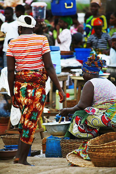 Full length of 20-29 years old african ethnicity / african-american ethnicity young women / female sitting / resting wearing headscarf / dress / traditional clothing who is smiling / happy / cheerful and holding mobile phone / using smart phone / text messaging / sitting on stool