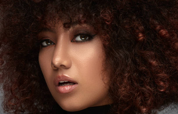 A smiling, curly-haired mulatto woman trying to stop herself from being photographed with her hand.