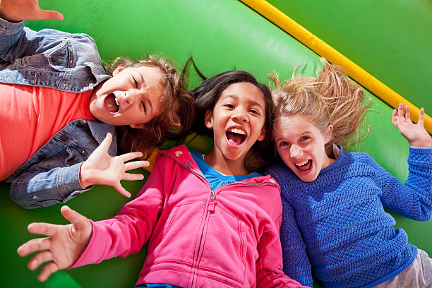 Girls lying down in bounce house Three multi-ethnic nine-year-old girls lie on their backs in an inflatable bouncy castle.  Their mouths are open, and the background is green. only girls stock pictures, royalty-free photos & images