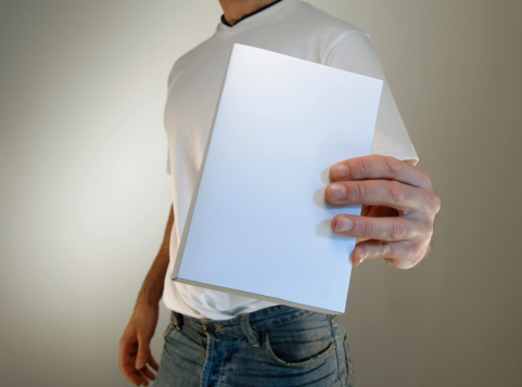 man in white t shirt and jeans holding up book with white empty book cover