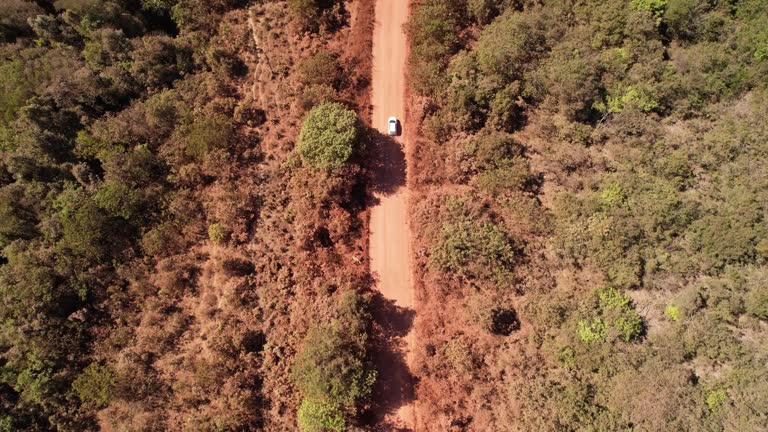 drone orbital view of a moving car raising dust on a dirt road in Chapada dos Veadeiros, Goiás, Brazil