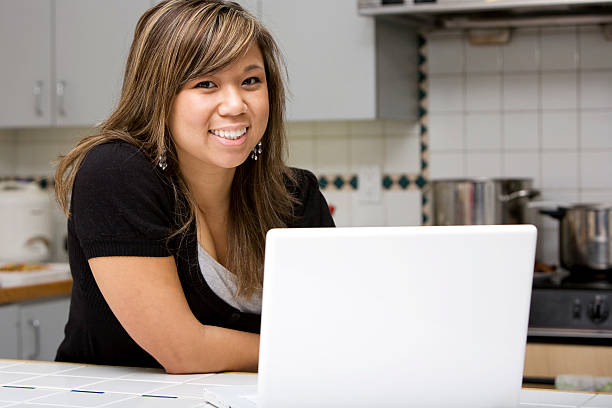 Asian Young Woman Using Laptop in Home Kitchen, Copy Space