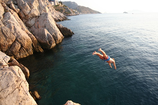 Millennial man is diving from a rock in the sea - Multiple images effect. Italy - Mediterranean sea during summer.