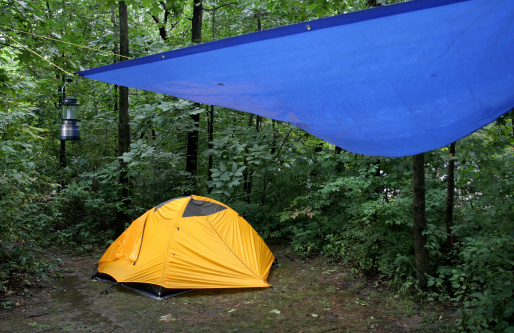 At a campground a yellow tent is set up with overhanging tarp for staying dry.  A camp lamp is ready for the night.