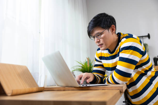istock Thai man wearing glasses using laptop and smiling at home. Reading email and working . Asian Man sitting working on laptop computer 1723426763