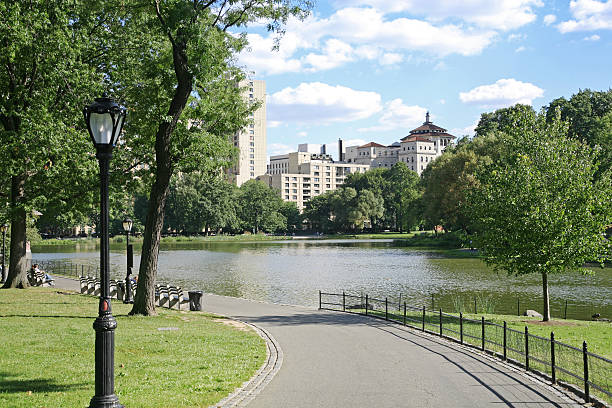 Harlem Meer And Skyline "Pedestrian footpath by lake, Central Park North, New York City, NY, USA." harlem park stock pictures, royalty-free photos & images