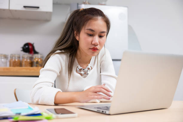istock Reading email and working. Asian thai young woman sitting working on laptop computer. Thai female using laptop and smiling at home 1723432214