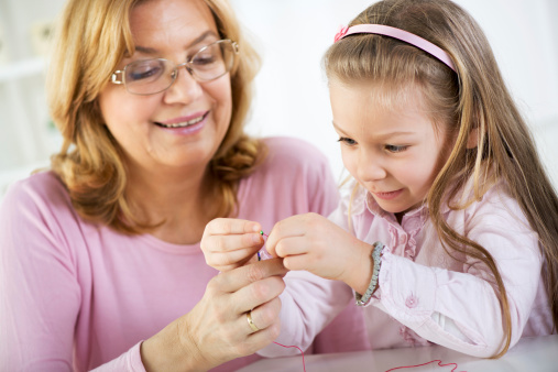 Young cute little girl making bead Jewelry with Grandmother.
