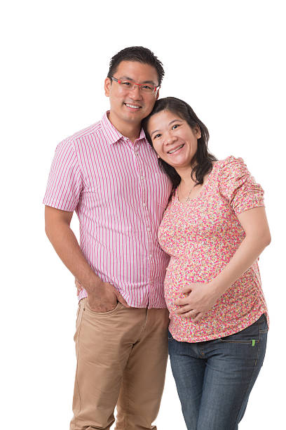 Young muscular man standing beside woman in an advanced state of pregnancy. Isolated on black background. Studio shot.