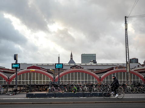 Copenhagen, Denmark - Oct 24, 2018: Front of the Copenhagen Central Station (Hovedbanegarden) on Tietgensgade. Bicycles parked on sidewalk. Cyclist (blurred) rides by. Overcast gloomy cloudscape.