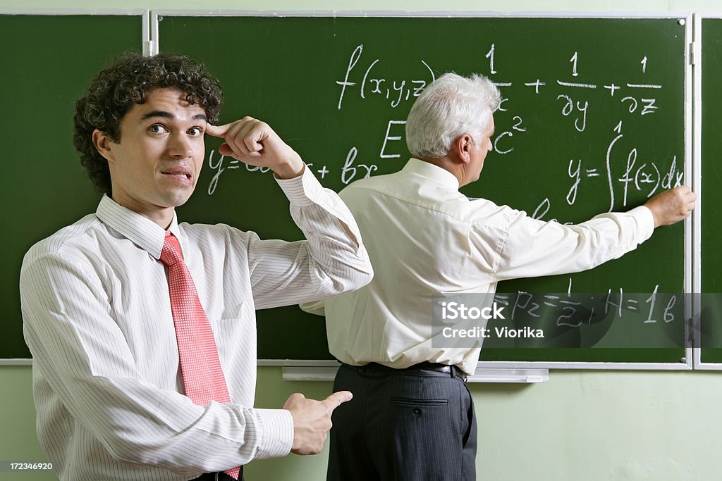 Mocking a professor Student mocking his lecturer behind his back while he is writing some formulas on the chalkboard. Active Lifestyle Stock Photo