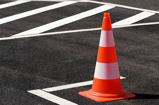 Orange traffic cone sitting on the black top pavement Traffic cone /pylon on a brand-new parking place. cone shape stock pictures, royalty-free photos & images