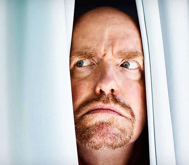 istock What is that? Suspicious man peeps through curtains, frowning 172347985
