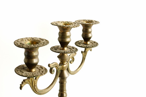 Horizontal closeup of an antique glass and pewter jug, a white candle in an antique silver candlestick and two fresh farm eggs in a decorative silver dish on a rustic wooden table.