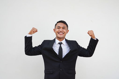 Portrait Young Asian businessman strong gesture, healthy and showing muscles, lifting his arm isolated on white background
