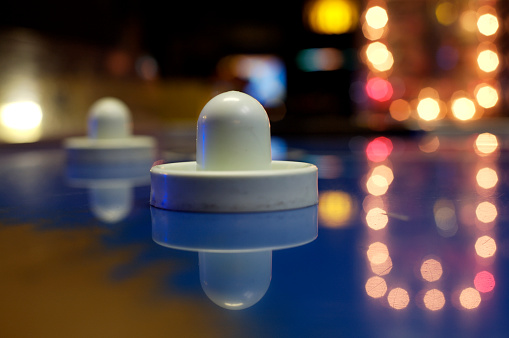 Closeup of an air hockey puck with shallow focus.  Defocused lights from other video games are in the background.
