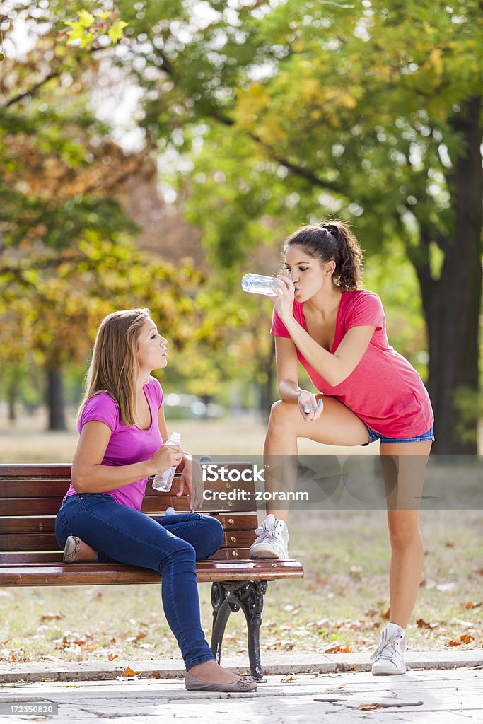 Drinking water "Two female friends at park, one of them is drinking bottled water" Adult Stock Photo