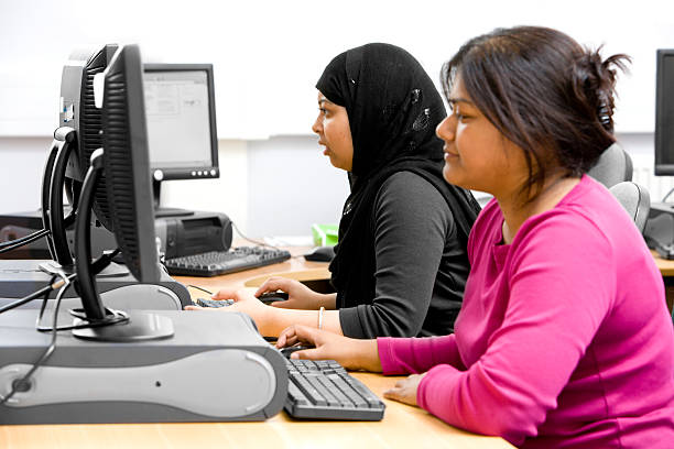 Two female college students use desktop computers. A pair of university students make use of their college's computer suite. school receptionist stock pictures, royalty-free photos & images