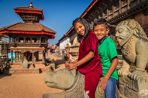 Children sitting on rhino sculpture, Siddhi Lakshmi Shikara Hindu temple in the Durbar square of Bhaktapur. Bhaktapur is an ancient town in the Kathmandu Valley and is listed as a World Heritage Site by UNESCO for its rich culture, temples, and wood, metal and stone artwork.