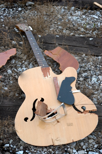Broken guitar lays on ground after being smashed.