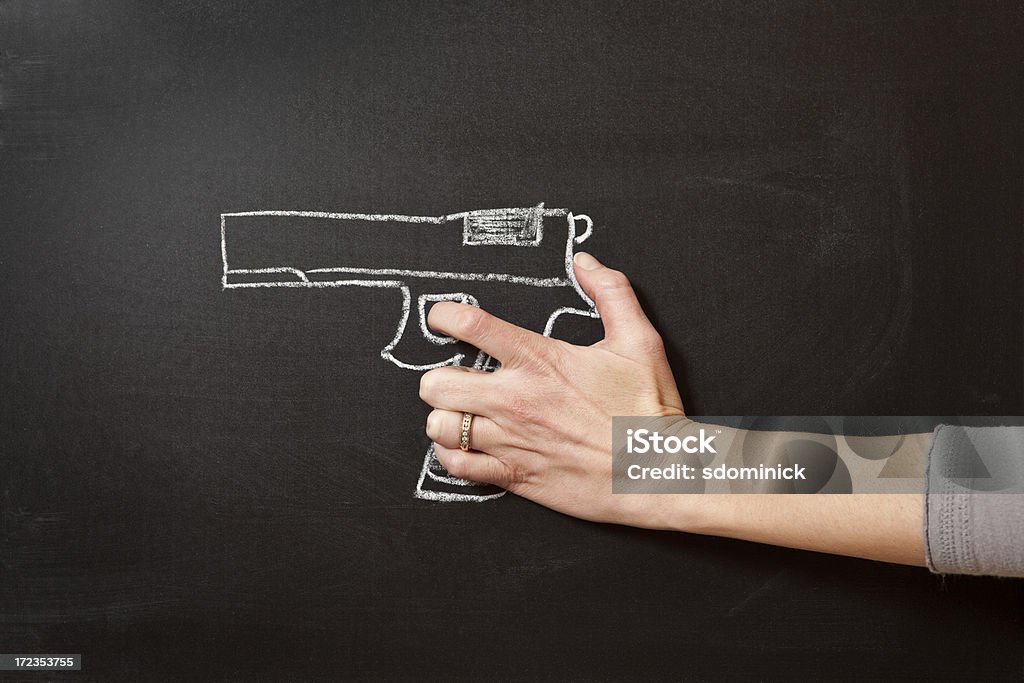 Hand Holding Chalk Drawn Gun The hand of a woman appearing to hold a chalkboard drawing of a hand gun. Drawing - Activity Stock Photo