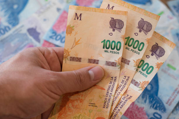 istock left hand holding thousand Argentine peso bills on blue banknotes background 1723538798