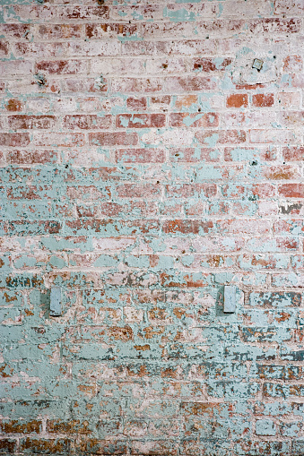An interior, red brick wall that has been painted numerous times, most recently with white and then green paint.