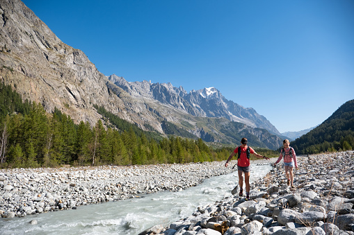 A young girl and her mother enjoy a hike outdoors along the river. Exploring the mountains near Courmayeur in Italy. Mother and daughter hiking together