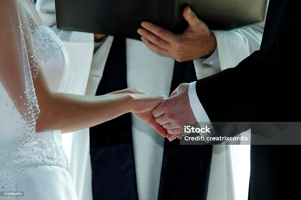 Groom holding a bride's hands on their wedding day bride and groom on their wedding day with priest in the background Wedding Stock Photo