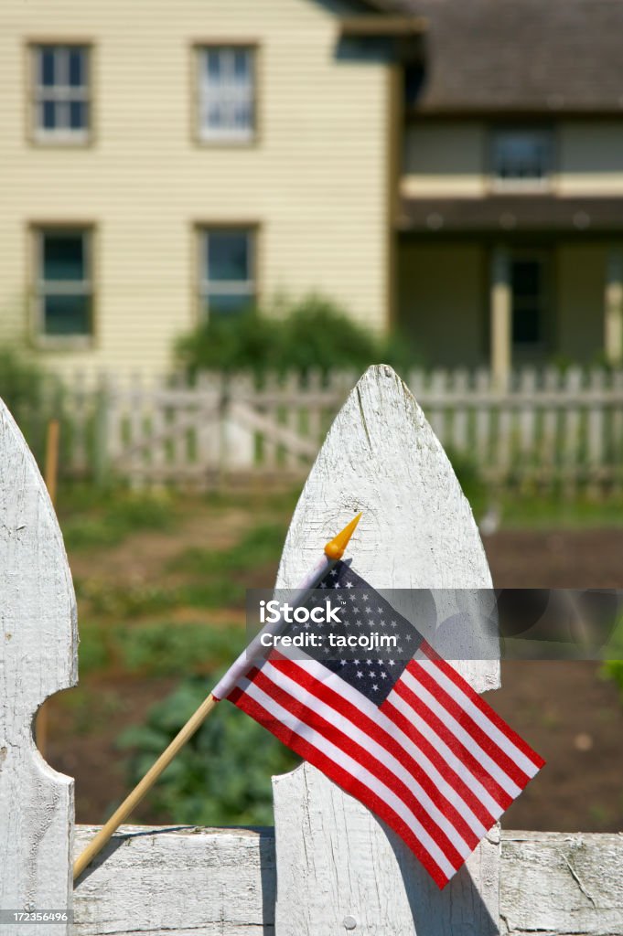 American Small American flag on a white picket fence in front of a farm house American Culture Stock Photo