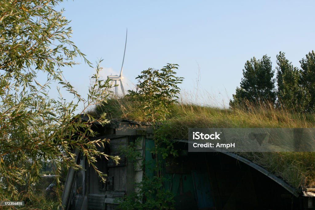 Green Living A house with grass as a roof and a wind turbine in the background. Wind Turbine Stock Photo