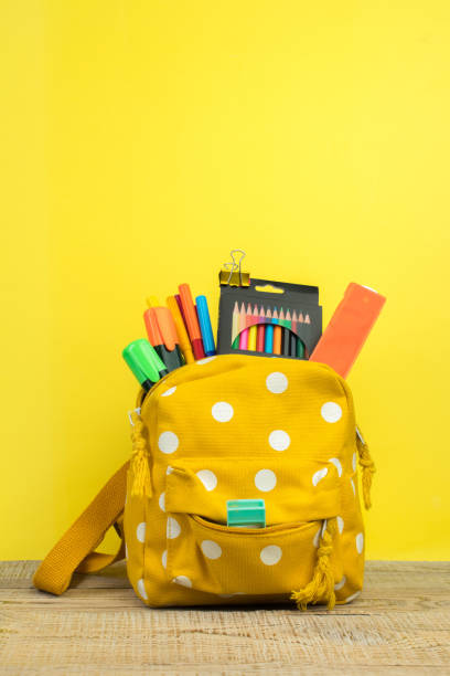 istock Yellow backpack with white polka dots with different colorful stationery on table. Yellow background. Back to school. 1723580303