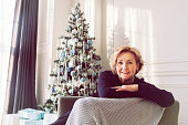 elderly smiling happy blonde woman is sitting in an armchair by the Christmas tree