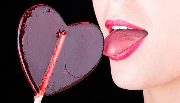 istock Girl licks heart lollipop on black background 172359376