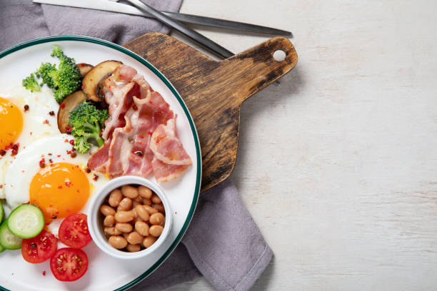 plato de desayuno tradicional englis con tiras de tocino, huevos soleados, verduras y pastel sobre fondo claro - englis fotografías e imágenes de stock