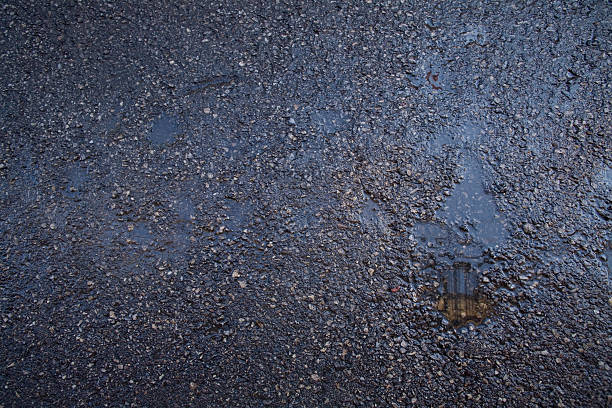 Wet black gravel road with puddles stock photo