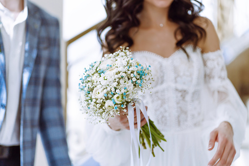 a young girl in a white wedding dress holds a bouquet of flowers and greenery with a ribbon in her hands