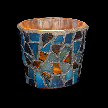 Candlelight glowing in the dark in colorful glass tiled mosaics holder.