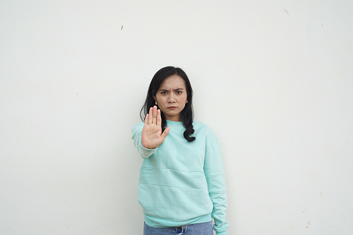 Portrait Indonesian beautiful woman wearing light blue sweater with stop and reject gesture isolated on white background