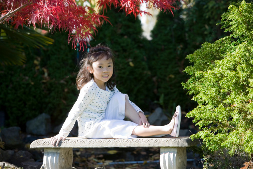 Little Asian girl sitting on a bench in the garden. Focus on face. CLICK FOR SIMILAR IMAGES AND LIGHTBOX WITH MORE CHILDREN.