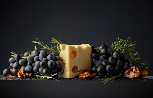 Maasdam cheese with walnuts, blue grapes, and rosemary on a black background.