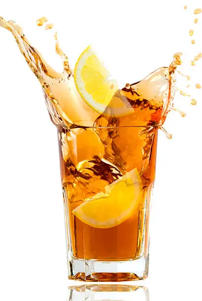 Lemon falling into a fresh icetea drink.the cold drink is spilling all through the air.perfect drink on a hot summer day.