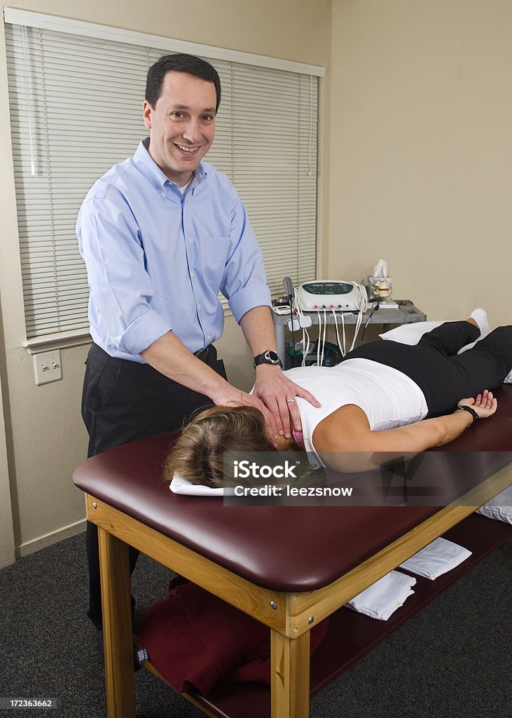 Physical Therapist Working On Neck Looking at Camera "Physical therapist (or chiropractor) looking at the camera with a smile while working on the neck of a patient.Click below for MORE IN THIS SERIES, plus all of my Physical Therapy and Chiropractic Treatment  images:" Adult Stock Photo