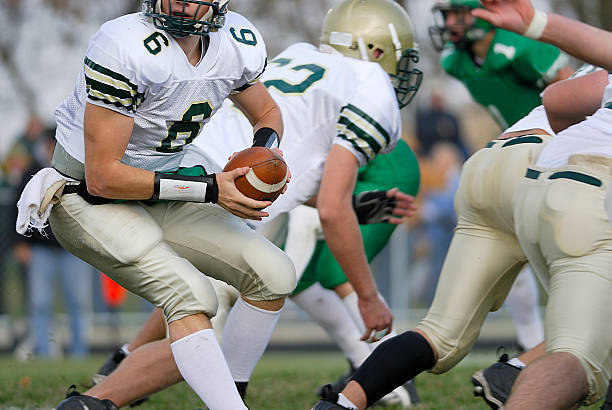 American football player in white dress and helmet holding a ball and looking for a free teammate.