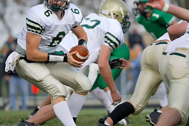 A american high school football quarterback turns to handoff the ball.
