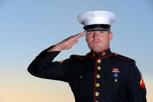 Male Marine In Dress Blues Uniform Saluting.  Sunset Background. 